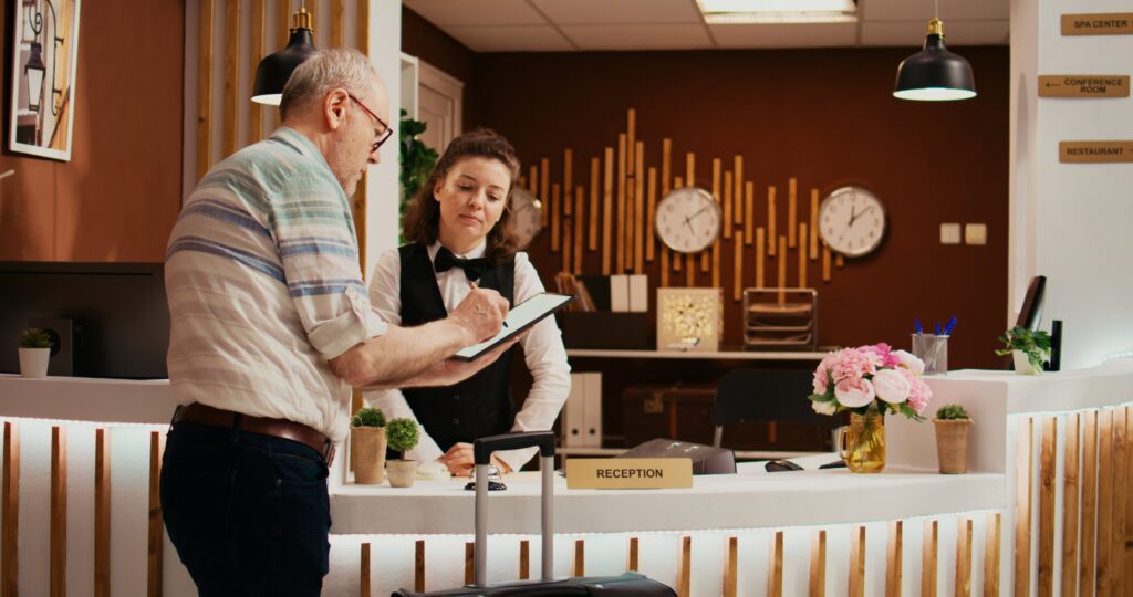 Old person signing documents at hotel reception to a receptionist